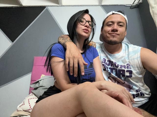 LucyAndJake with black hair and glasses, wearing a blue shirt, sits with her arm around Jake, who's in a white backward cap and blue tie-dye shirt.