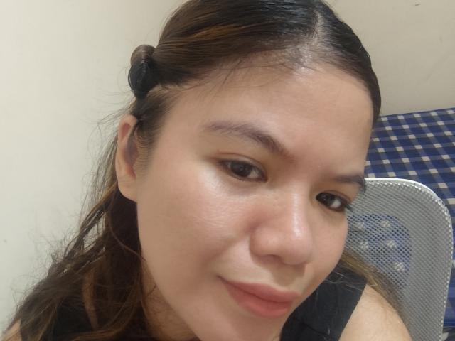 CherAgatha has tan skin, brown eyes, and a slight smile with a black hair clip on the right side. Her face is close to the camera, showing a bit of her chest.