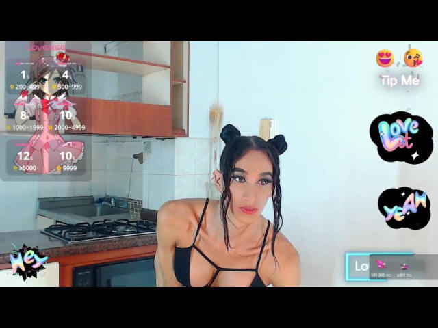 SofiaHornnys with black bikini top, small black cat ears, and long dark hair, leaning forward in a kitchen, showing off her big tits and cute face.