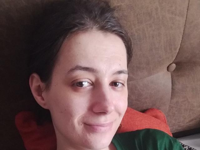 JuliaHuntis has a cute, slightly smug face with brown eyes, short dark hair, and a small smile. She's lying on a brown couch with a red pillow.
