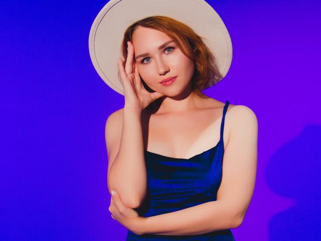 TeresaBirt with red hair, wearing a white hat and blue velvet dress, touching her face, showing her tits, against a purple background, looking cute and sexy.