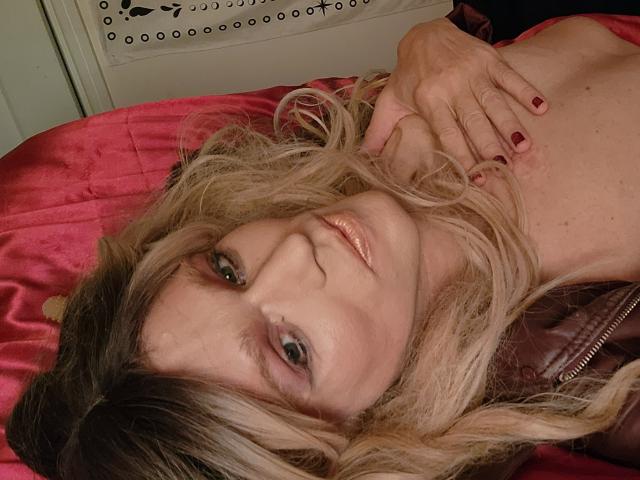 Jeunes femmes aux cheveux blonds, allongées sur un lit rouge, seins nus, main sur la poitrine, lèvres brillantes, ongles rouges, regardant la caméra, sourire doux, légère rougeur, seins visibles..