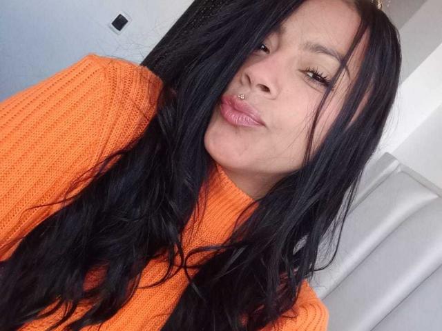 Amberv with long black hair, orange knit sweater, and nose ring, puckering lips slightly, showing off her pouty ass-kissing lips.