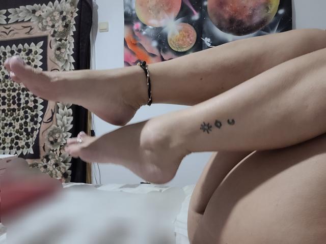 BarbaraBowie's legs are crossed, showing her bare feet with a black anklet and small tattoos on her right ankle. Her pussy is partially visible in the lower right.