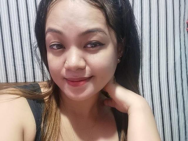 PinaylhianForU has light skin, brown eyes with winged eyeliner, and a small nose ring. She's smiling with a hand near her neck, wearing a black top.