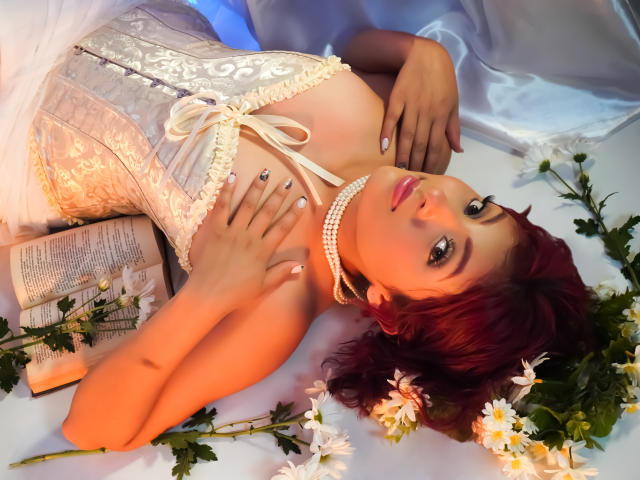 LizBonnet with red hair, wearing a white lace corset and pearl necklace, lying on flowers, hands on her tits, book under her, glowing orange light, sexy look.