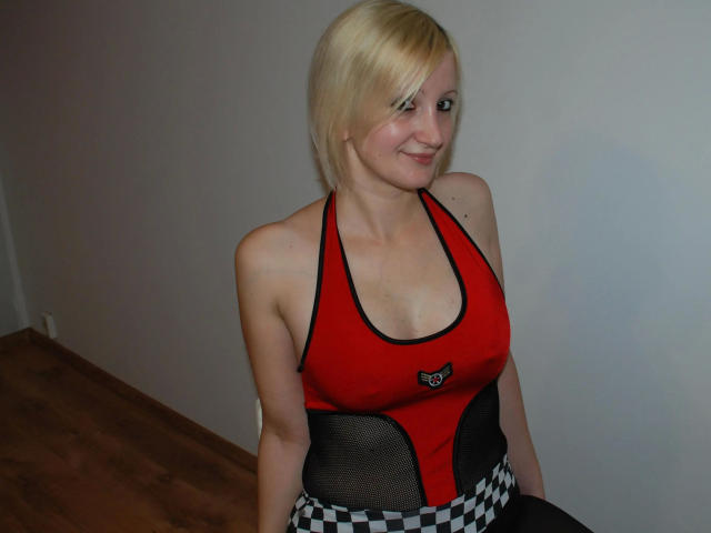 HotTitts-hot with blonde hair, red and black sports top, showing her small tits, smiling, sitting on wooden floor, wearing checkered black and white skirt.