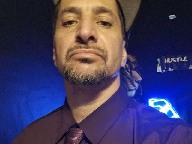 SnackPants has a light brown beard, mustache, and wears a brown shirt with a maroon tie. He's also sporting a beige hat. His face is slightly out of focus.