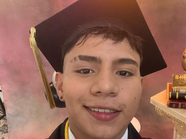 RichiMontes, wearing a black graduation cap with a gold tassel, has short brown hair, dark eyebrows, small moles on the nose, and a pinkish smile. RichiMontes has small earrings.