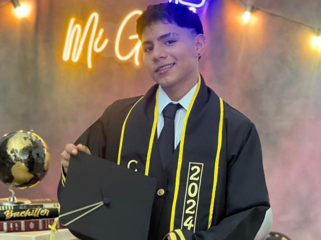 RichiMontes in een zwarte afstudeerkleding met gele biezen, met een zwarte muts in de hand, lachend, met een zwarte das, met een globe-award in de hand, een neonbord met "Mr. G" op de achtergrond..