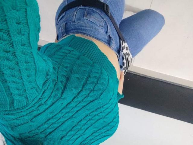 Kkatalina's green, cable-knit sweater, showing her ass in tight blue jeans, with a black belt and white sneakers, taken from a high-angle, rear-view shot.