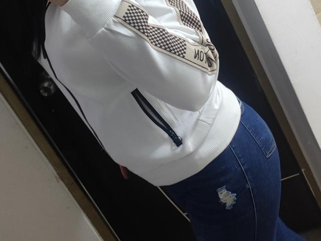 Kkatalina with a white hoodie, arms crossed, showing a small ass in tight blue jeans with a hole on the right buttcheek. Hoodie has black and white patterns.