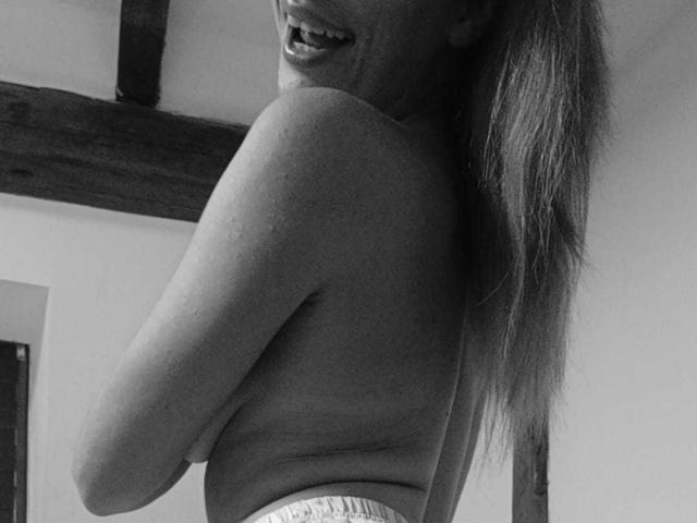 Black-and-white photo of IngridI with her back to the camera, long hair, smiling, wearing a tight shirt, showing her ass, and a visible waistband.
