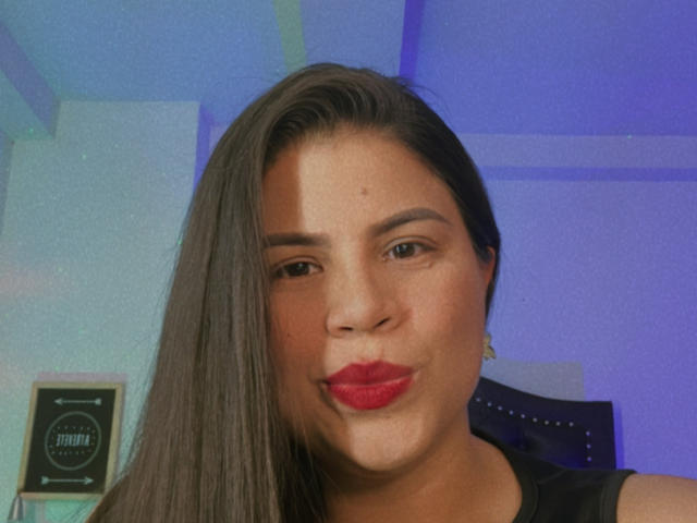 LaliForest, con le labbra rosse e i lunghi capelli castani, stringe i glutei in un selfie, indossando una maglietta nera, e ha la pelle color nocciola e piccoli orecchini..