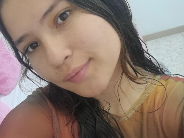 CelesteDash has wet black hair, brown eyes, and a slight smile. She's wearing a brown shirt with pink and red accents. Her nose is small, and her lips are pink.