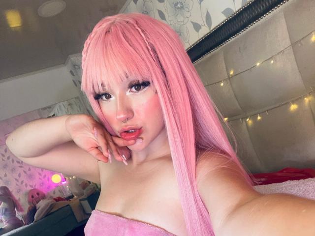 CristySanz with pink hair, pouty lips, and long eyelashes, holding her finger to her mouth, wearing a pink towel, showing her tits, in a cute, pink-themed bedroom.