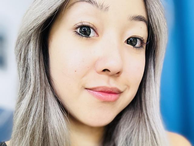 RenyLime's face with light gray hair, green eyes, subtle pink lipstick, and a small beauty mark near her nose. She's smiling softly, showing a cute, natural look.