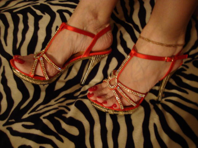 I tacchi rossi di HappyLady69, con cinturini e borchie dorate, e le dita dei piedi dipinte di rosso, su una superficie a motivi zebrati. Le sue caviglie sono adornate da delicati braccialetti dorati..