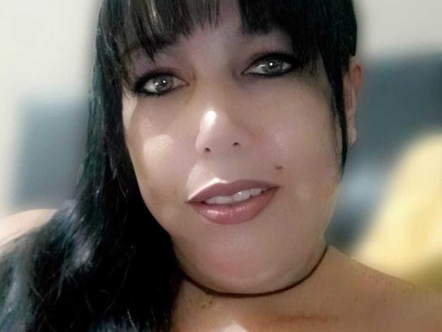 NatashaOlg has dark black hair, green eyes, and a slight smile. She has small moles on her right cheek and a choker. Her lips are shiny and pink.