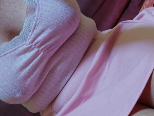 A blusa rosa canelada de LylyCoquine69, com detalhes em renda, cobrindo seus seios, e uma saia rosa, que mostra sua cintura e parte de suas nádegas. Macia, rosa e ligeiramente amassada..