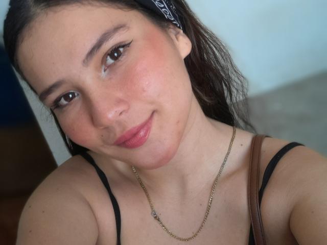 CelesteDash has medium tits, a cute nose piercing, brown eyes, and a slight smile. She's wearing a black top, a chain necklace, and a headband in a selfie.