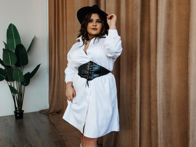 DreamForeYou with big tits, wearing a white dress, black corset, and black hat, standing by brown curtains, holding hat, with puffy ass, and brown skin, and curly hair.