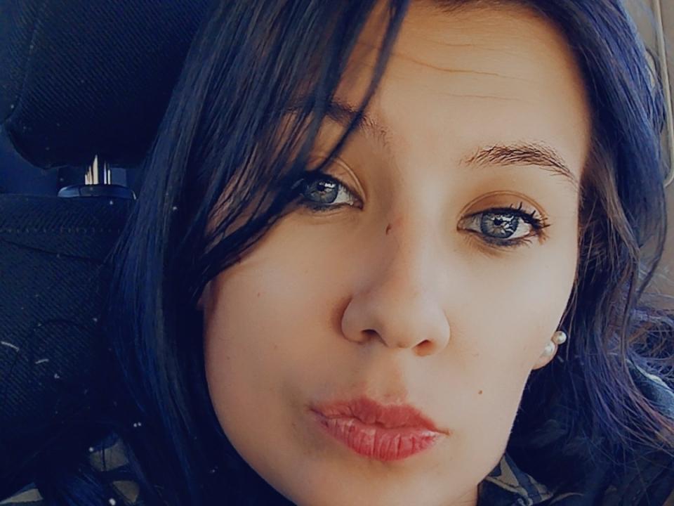HotBebedux has blue eyes, dark straight hair, light skin, small nose, and pouty red lips. She's making a puckered face in a car with a black headrest.