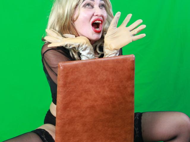 SURRENDER-hot with blonde hair, red lipstick, black sheer top, black lingerie, and tan gloves, screaming with arms raised, holding a brown leather box in front of her.