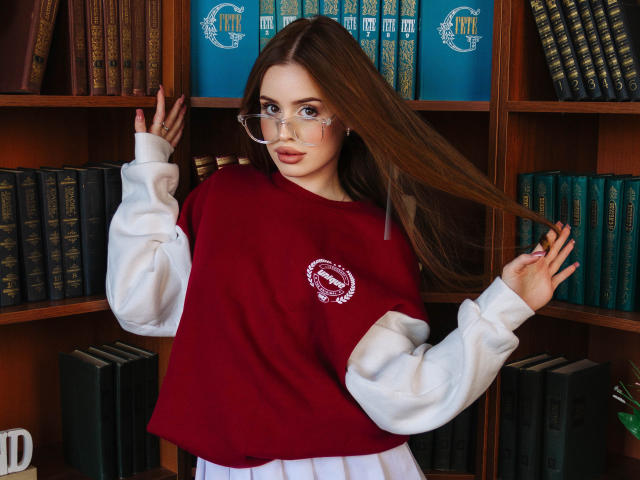 CherylFoxy with long brown hair, wearing glasses, red sweater, white sleeves, white skirt, holding hair, bookshelf in background, looking at camera, cute, sexy.