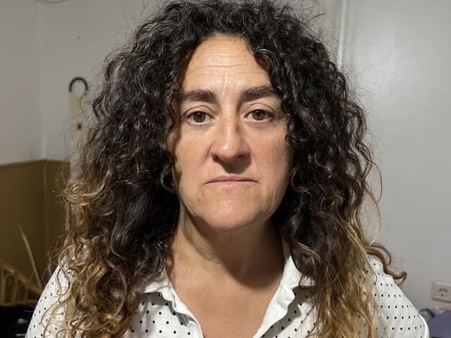 TuFavoritaMilf has curly black and blonde ombre hair, light skin, brown eyes, and a neutral expression. She's wearing a white polka dot shirt. Her face is slightly wrinkled.