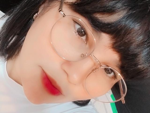 PrittyAlicia has round glasses, black bangs, and shiny black hair. She's wearing a white shirt with red lips. Her face is slightly tilted, showing a cute, soft expression.