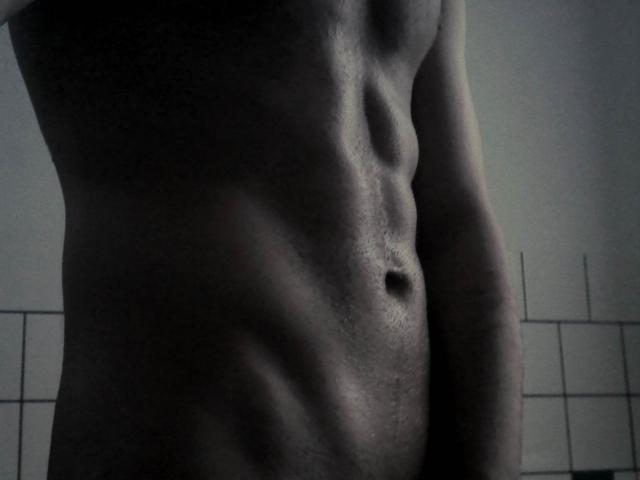 A black-and-white shot of BigJohnDee's toned, muscular abs and chest, with a visible navel and slight shadow, showing defined muscles and a smooth, dark skin texture.