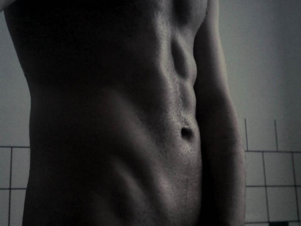 A black-and-white shot of BigJohnDee's toned, muscular abs and chest, with a visible navel and slight shadow, showing defined muscles and a smooth, dark skin texture.