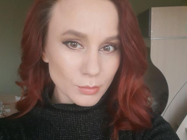KristiVegas has red hair, light skin, and is making a puckering face. She's wearing a black, textured top, with subtle makeup and brown eyes.