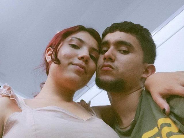 SpecialFriendsBenefits with red hair, small tits, and a pink top, and SpecialFriendsBenefits with dark hair, a goatee, and a green shirt, standing close and looking at the camera.