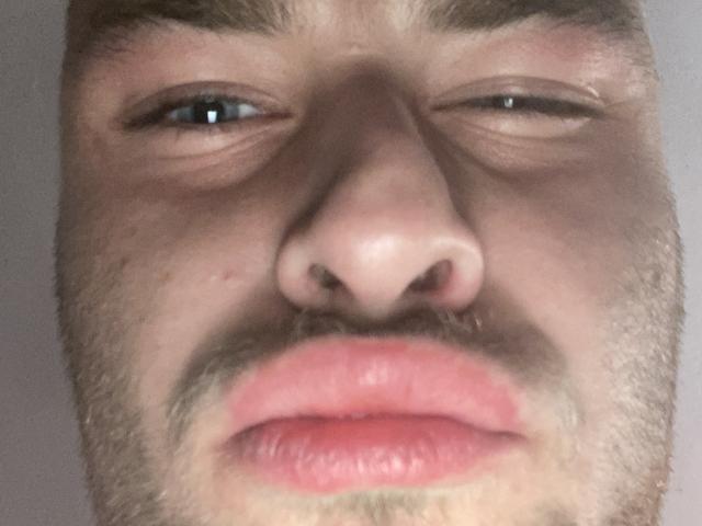 PsedobiDan's face with slightly squinted eyes, brown eyebrows, light skin, small nose, and pinkish lips. He's looking down with a neutral expression, showing some facial stubble.