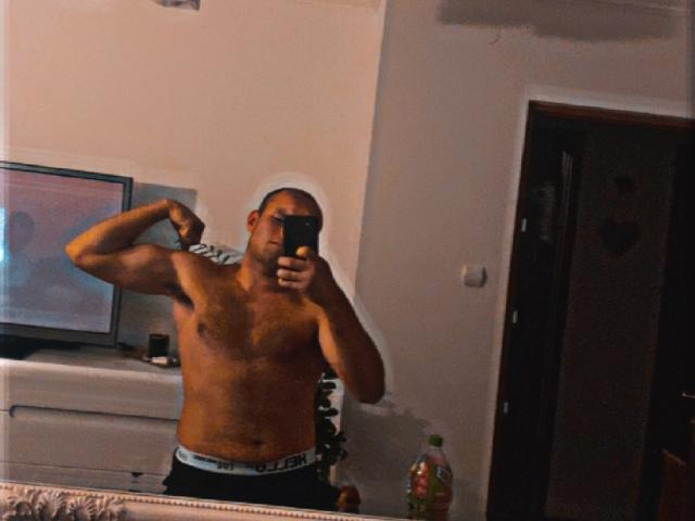PsedobiDan, shirtless with a muscular build, flexes his right arm in a mirror selfie, wearing black boxer briefs, holding a phone, in a dimly lit room.