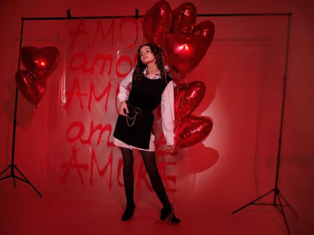 Letty Curly, met donker krullend haar, draagt een zwarte jurk over een witte blouse, zwarte leggings en zwarte laarzen, en staat met rode hartvormige ballonnen, rode verlichting en een zelfverzekerde pose..