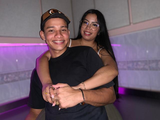 SaraAndMoreno with long black hair, glasses, and tan skin, hugs a smiling Latino dude with a cap, black shirt, and tan skin, her hands on his ass.