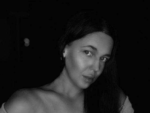 Black-and-white photo of FinessiaLovely with long dark hair, bare shoulders, and a slight smile, looking to the side with soft, shiny skin and subtle makeup.