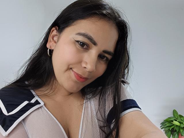 SofiaCopers has long black hair, brown eyes, and a slight smile. She's wearing a sheer top with navy and white trim, showing her small tits. She has a hoop earring.