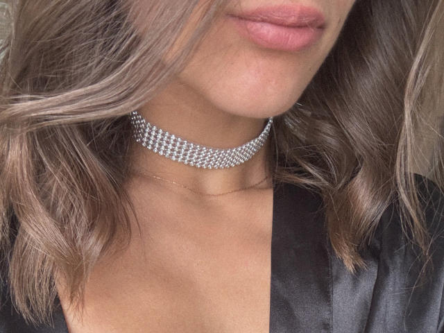 Pingli's face, with pouty pink lips, wearing a sparkly diamond choker and a black satin robe, has wavy brown hair. Her bare shoulders are visible.