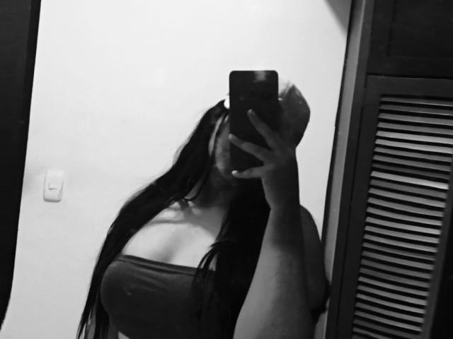 Black-and-white selfie of AmaliaDalton with long dark hair, holding a phone covering her face, wearing a strapless top showing her big tits, standing in front of a mirror.