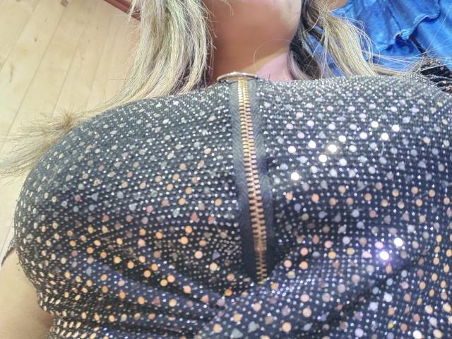 Contelaya's huge tits are covered in a black, sparkly, zipped-up top, showing off tiny glittery dots and a gold zipper running vertically down the middle.