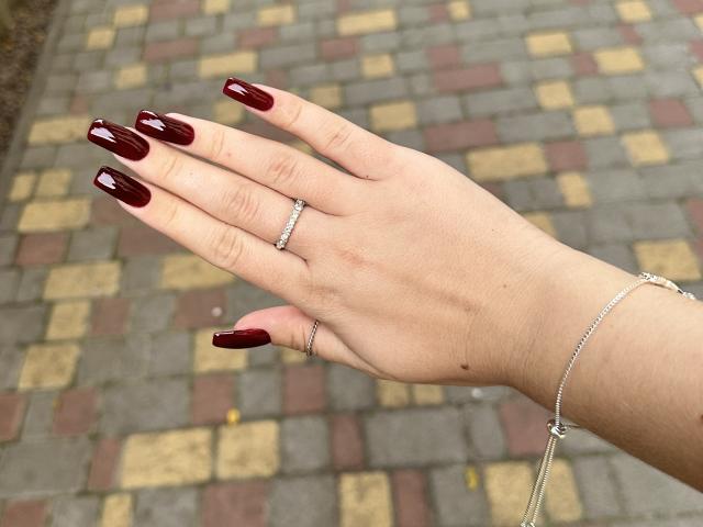La mano di SugarrX, con unghie laccate di un rosso scuro intenso, un anello d'argento e un delicato braccialetto a catena, che mette in risalto un piccolo diamante. Pelle chiara, con vene leggermente visibili al polso..