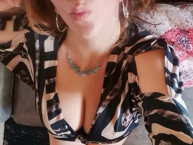 HotPamelaSex with her big boobs, wearing a black and white striped dress with cutouts, silver necklace, and hoop earrings, pouting her lips. Her brown hair is partially visible.