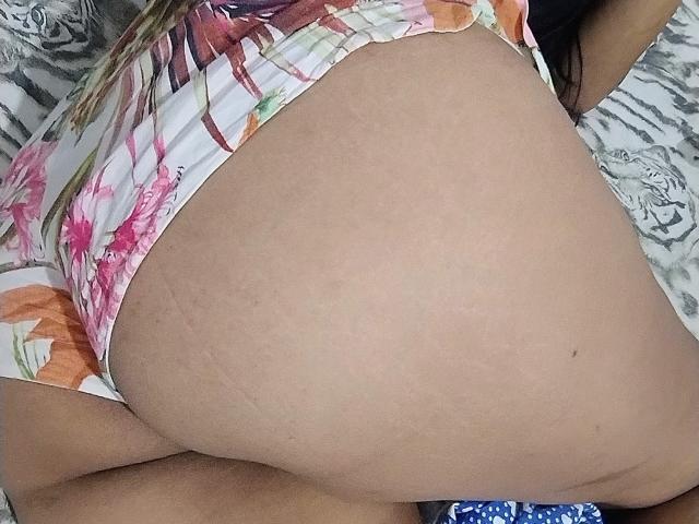 FlorLuna69's butt in floral underwear, showing a tan, slightly stretched, and smooth ass with visible stretch marks, lying on a patterned bed.