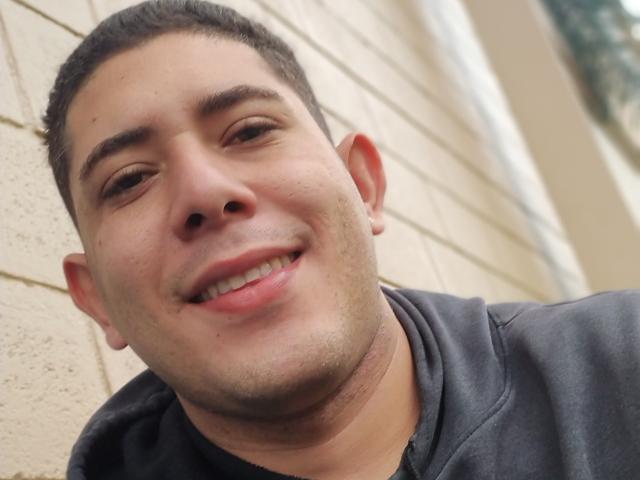 AjacHot has a cute, slightly chubby face with short dark hair, a small nose, and a gentle smile. He's wearing a gray hoodie, looking slightly tilted.