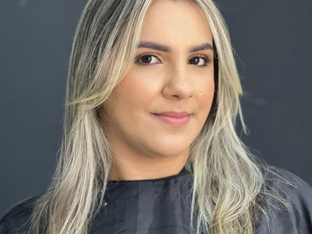 Karenmy has blonde, wavy hair, brown eyes, and a slight smile. She's wearing a black top, and her skin is light with a natural, subtle makeup look.
