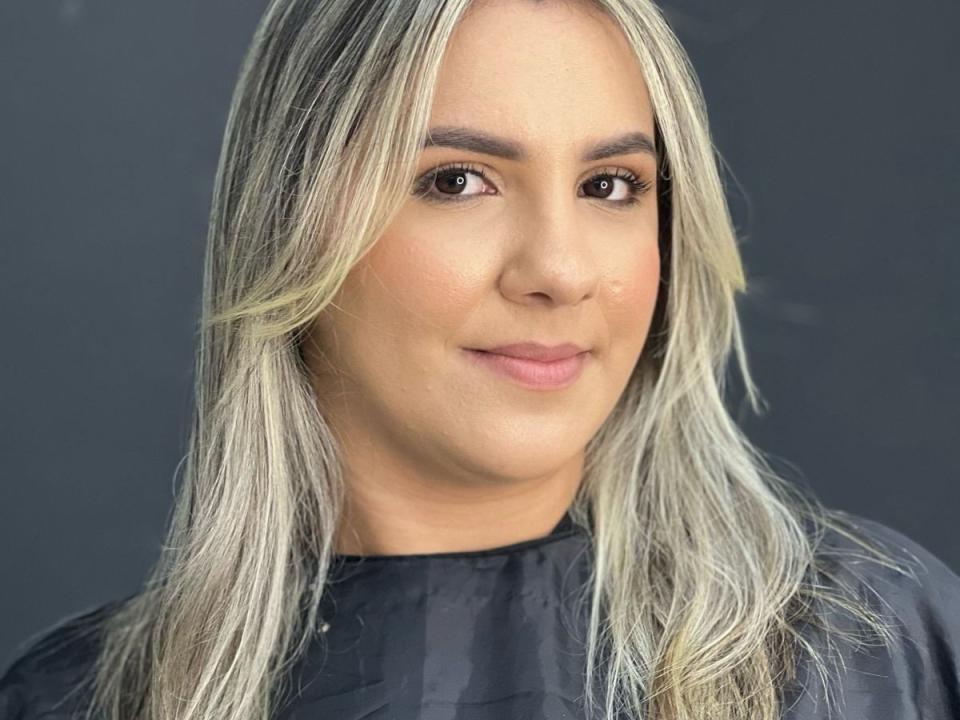 Karenmy heeft blond, golvend haar, bruine ogen en een lichte glimlach. Ze draagt een zwarte top, en haar huid is licht met een natuurlijke, subtiele make-up look..